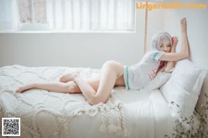 A woman sitting on a bed in a white room.