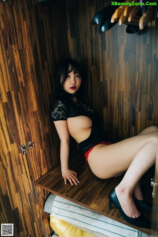 A woman sitting on top of a wooden shelf in a closet.