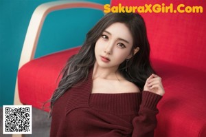 A woman sitting on the floor in a red sweater.