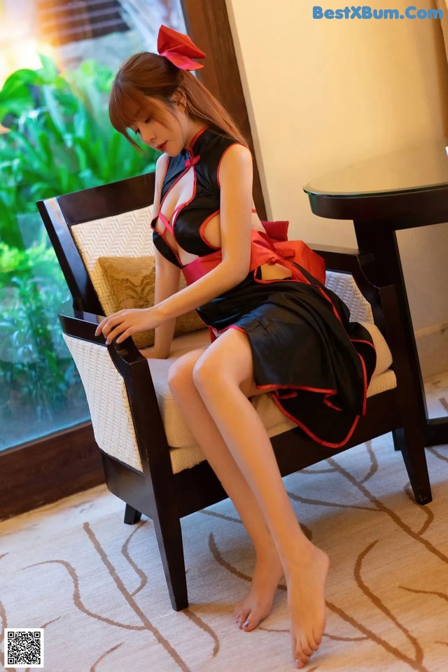 A woman in a black and red dress sitting on a chair.