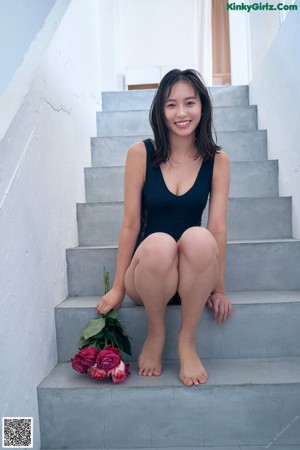 A woman in a black bodysuit holding a bunch of pink roses.