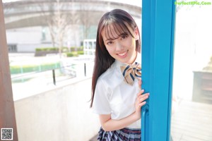 A young woman in a school uniform leaning against a wall.