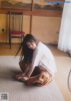 A woman with long brown hair standing in front of a window.