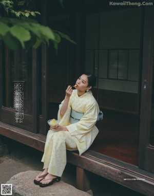 A woman in a blue and white kimono sitting on a wooden bench.