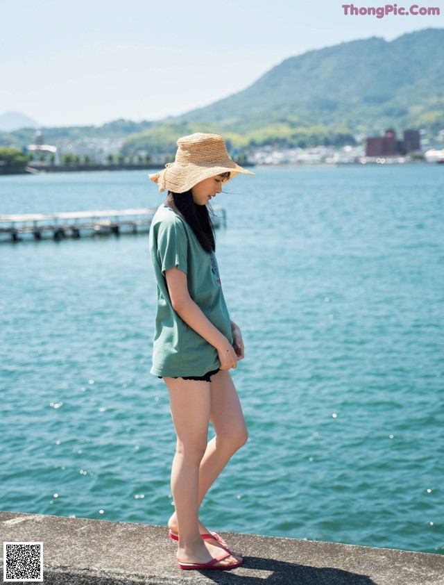 A woman wearing a straw hat standing by the water.