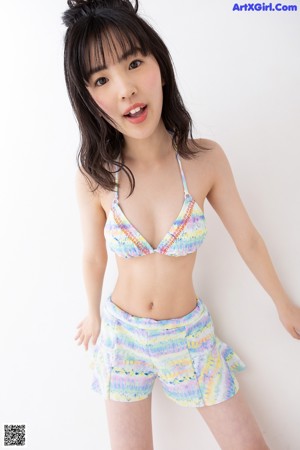 A woman in a bikini top and shorts standing in front of a white background.