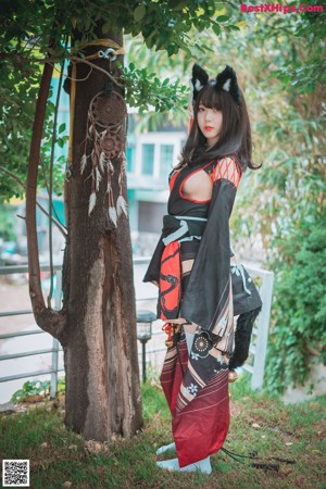 A woman in a black and red kimono sitting on the grass.