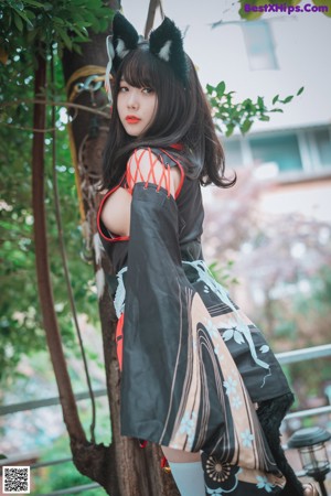 A woman in a kimono posing next to a tree.