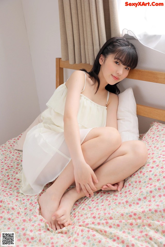 A woman sitting on a bed in a white dress.
