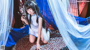 A woman in a white and blue outfit sitting on a bed.