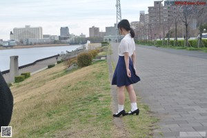 A woman in a white shirt and blue skirt standing next to a fence.